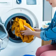 Ręce wkładają żółtą koszulę do pralki. Tak właśnie prac len, by był świeży i pachnący.