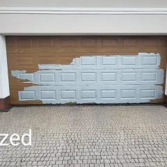 Brama garażowa w trakcie wymiany okleiny. Widoczna stara, brązowa okleina i fragmenty nowej, szarej.