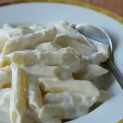 Penne w kremowym sosie serowym, idealne na słodko. Łyżka czeka, by zanurzyć się w tej pyszności.