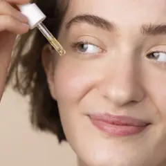 Delikatna skóra młodej kobiety otrzymuje kroplę cennego serum z retinolem do twarzy.