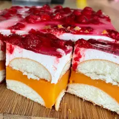 Pyszne ciasto z biszkoptami, pomarańczową galaretką i bitą śmietaną, ozdobione malinami.