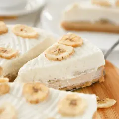 Kawałki ciasta bananowego bez pieczenia, ozdobione plasterkami suszonego banana, na drewnianej desce.