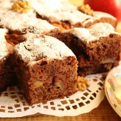 Pyszne ciasto cynamonowe z jabłkami, posypane cukrem pudrem i orzechami. Obok filiżanka herbaty i jabłka.