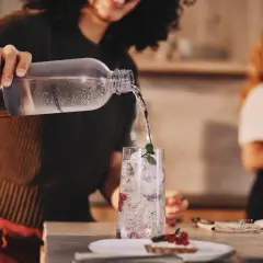 Przygotowanie efektownej kolacji dla znajomych. Nalewanie wody do szklanki z lodem i owocami.