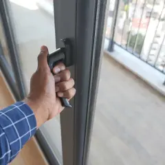 Dłoń chwyta za klamkę, wykonując regulację drzwi balkonowych. Widok na balustradę i miasto.