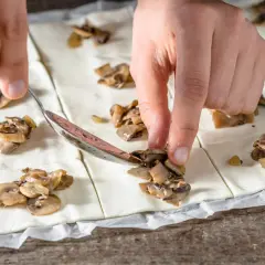 Ręce układają pieczarki na cieście francuskim, przygotowując pyszne przekąski.