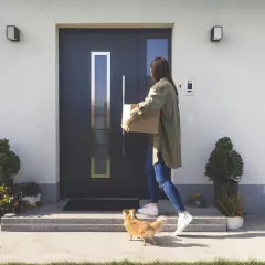 Elewacja wokół drzwi wejściowych z nowoczesnym domofonem. Kobieta z paczką i piesek witają się przy wejściu.