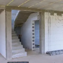Wnętrze budowy z betonowymi schodami i pustakami. Widoczna ościeżnica stała wymiary, przygotowana do montażu drzwi.