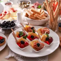 Pyszne menu na urodziny w domu: tartaletki z owocami, przekąski z szynką i oliwkami, sery, grissini i ciasto.