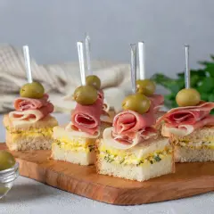 Mini kanapki z szynką, oliwkami i pastą jajeczną na desce.