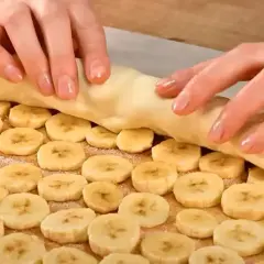 Ręce zwijają ciasto francuskie z bananem, tworząc pyszny deser.