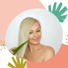 Blondynka z uśmiechem dotyka swoich włosów liściem aloesu, który jest naturalnym kosmetykiem do pielęgnacji włosów.