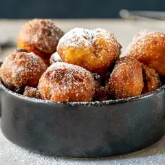 Puszyste paczki z serka homo, posypane cukrem pudrem, kuszą swoim złotym kolorem i apetycznym wyglądem.