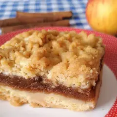 Pyszny kawałek szarlotki bez cukru z jabłkami i cynamonem, na talerzyku w kropki. Obok jabłko i laski cynamonu.