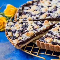 Prosta tarta z budyniem czekoladowym i jagodami, posypana kruszonką. Obok żółte róże.
