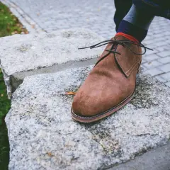 Brązowy zamszowy but na kamiennym murku. Dowiedz się, czym czyścić zamsz, by wyglądał jak nowy.