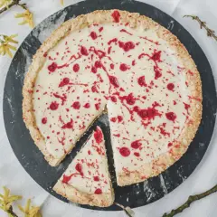 Pyszny mazurek z białą czekoladą, ozdobiony malinowym sosem, na tle wiosennych gałązek.