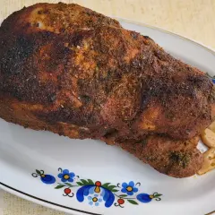 Pieczona łopatka wieprzowa z czosnkiem, przyprawiona ziołami, na talerzu z ludowym wzorem.