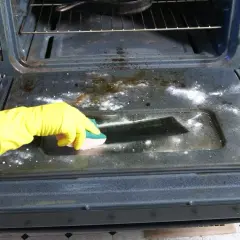 Rękawica w żółtej rękawicy czyści piekarnik z przypalonego tłuszczu. Soda oczyszczona i gąbka pomagają w tym zadaniu.