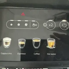 Ekspres DeLonghi z czerwoną kontrolką ostrzegawczą. Widoczne ikony napojów: latte, cappuccino, espresso, kawa, gorąca woda.
