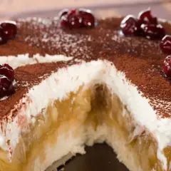 Szarlotka bez pieczenia na herbatnikach z budyniem, udekorowana wiśniami i kakao. Pyszny deser, który zachwyca smakiem.