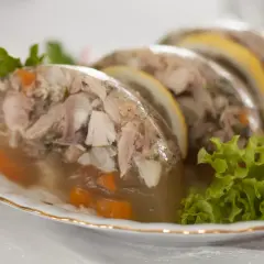 Pyszne nóżki w galarecie z kawałkami mięsa, marchewką i plasterkami cytryny, ozdobione natką pietruszki i sałatą.