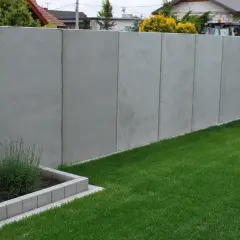 Nowy, wysoki, betonowy płot stanowi pełne ogrodzenie od sąsiada, oddzielając dwie posesje.