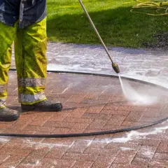 Osoba w zielonych spodniach czyści kostkę brukową myjką ciśnieniową, usuwając stare plamy z oleju.