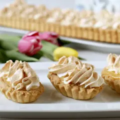 Słodkie babeczki z bezą, idealne, gdy zastanawiasz się, co można zrobić z żółtek. W tle duża tarta i tulipany.