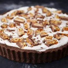 Czekoladowa tarta z kajmakiem i mascarpone, udekorowana kawałkami batoników.