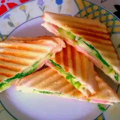 Chrupiące tosty z szynką, serem i świeżym ogórkiem na talerzu z kolorowym wzorem. Idealne na szybki lunch.
