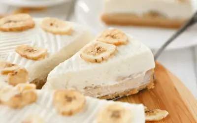 Kawałki ciasta bananowego bez pieczenia, ozdobione plasterkami suszonego banana, na drewnianej desce.
