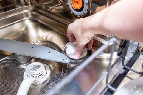 Dłoń zakręca białą nakrętkę, pokazując, gdzie wsypać sól do zmywarki.