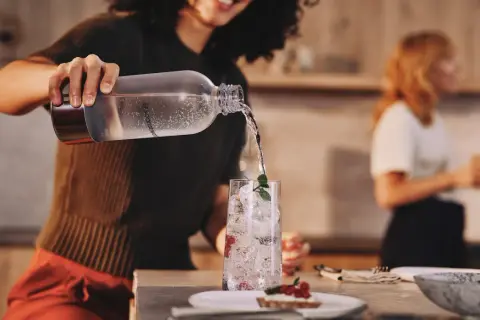 Przygotowanie efektownej kolacji dla znajomych. Nalewanie wody do szklanki z lodem i owocami.