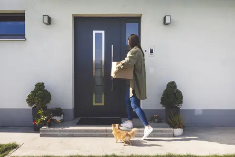 Elewacja wokół drzwi wejściowych z nowoczesnym domofonem. Kobieta z paczką i piesek witają się przy wejściu.