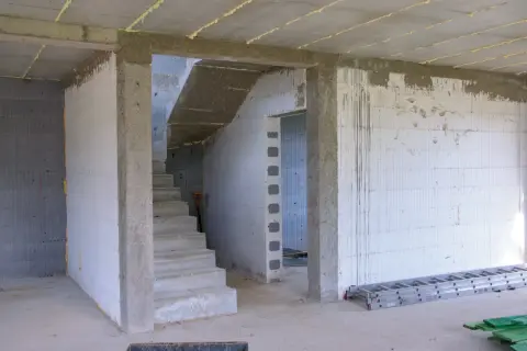 Wnętrze budowy z betonowymi schodami i pustakami. Widoczna ościeżnica stała wymiary, przygotowana do montażu drzwi.