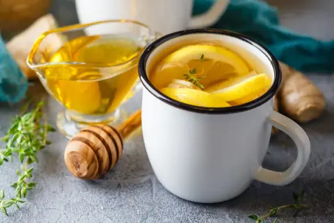 Rozgrzewający napar z imbiru z cytryną i miodem, idealny na chłodne dni. Obok sosjerka z płynnym złotem i świeże zioła.