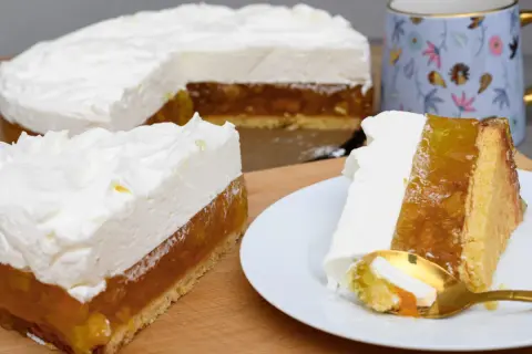 Pyszne ciasto z bitą śmietaną i galaretką owocową. Na talerzyku kawałek z widelczykiem, obok cały deser.