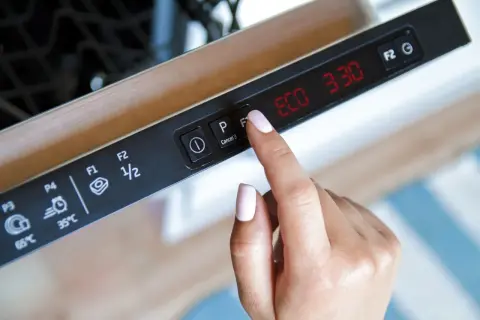 Dłoń naciska przycisk F1 na panelu zmywarki, wybierając symbol mycia w zmywarce. Na wyświetlaczu ECO 3:30.
