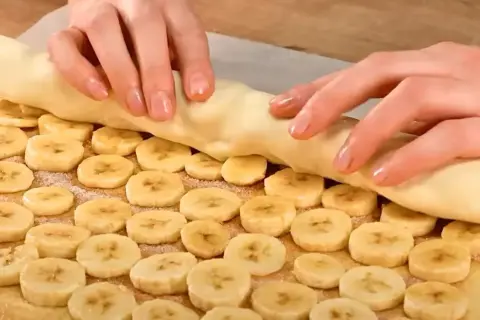 Ręce zwijają ciasto francuskie z bananem, tworząc pyszny deser.