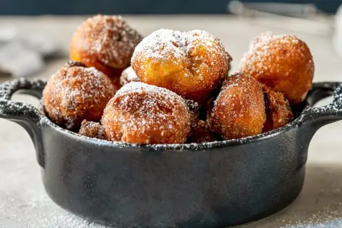 Puszyste paczki z serka homo, posypane cukrem pudrem, kuszą swoim złotym kolorem i apetycznym wyglądem.