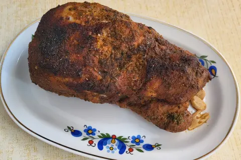 Pieczona łopatka wieprzowa z czosnkiem, przyprawiona ziołami, na talerzu z ludowym wzorem.