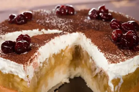 Szarlotka bez pieczenia na herbatnikach z budyniem, udekorowana wiśniami i kakao. Pyszny deser, który zachwyca smakiem.