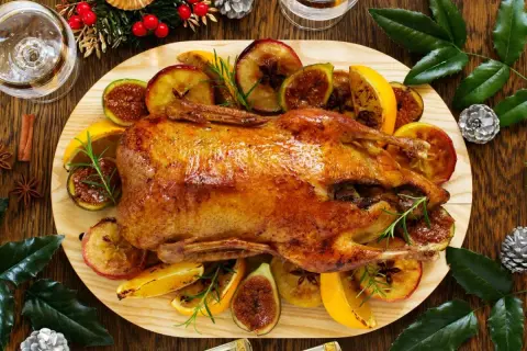 Pieczona kaczka z jabłkami, figami i pomarańczami na drewnianej desce.
