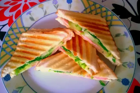 Chrupiące tosty z szynką, serem i świeżym ogórkiem na talerzu z kolorowym wzorem. Idealne na szybki lunch.