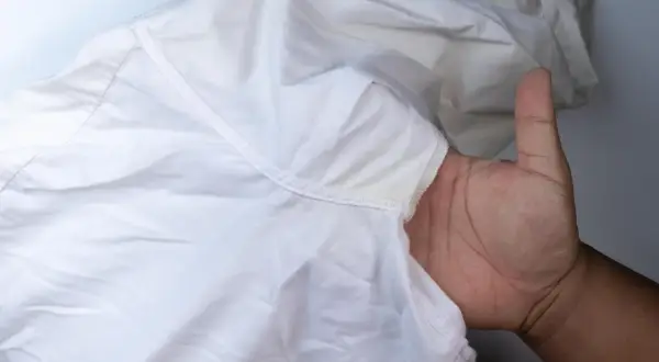Dłoń pokazuje białą koszulę z żółtymi, twardymi plamami po antyperspirancie pod pachą.