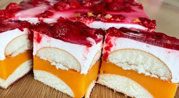 Pyszne ciasto z biszkoptami, pomarańczową galaretką i bitą śmietaną, ozdobione malinami.