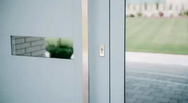 Nowoczesne drzwi wejściowe z metalową klamką i wizjerem. Widoczna regulacja drzwi wejściowych, zapewniająca płynne domykanie.