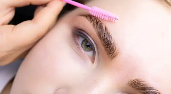 Stylist czesze brwi szczoteczką po zabiegu laminacji. Zabieg można powtarzać co 4-6 tygodni.