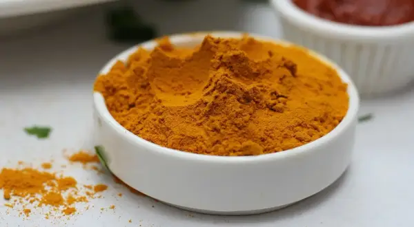 Jasnożółta kurkuma w proszku w białej miseczce, idealna do curry, zup i napojów. Kurkuma do czego? Do zdrowia i smaku!